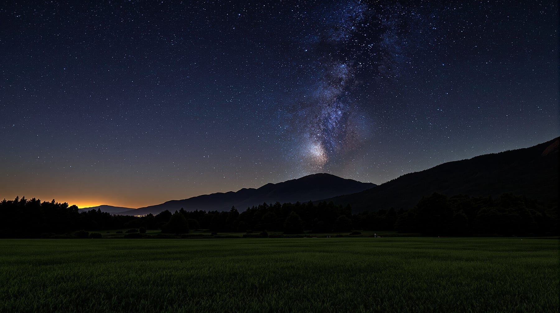 Open dark observing field at the foot of a forested mountain under a star-filled sky