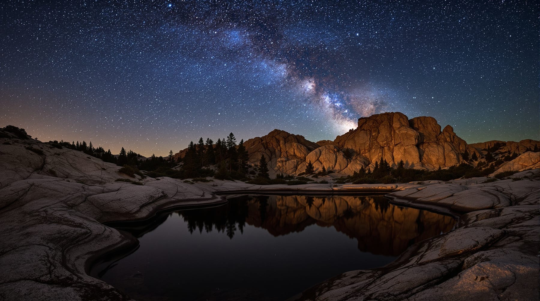 Bare granite barrens and a still pond under a dense star field