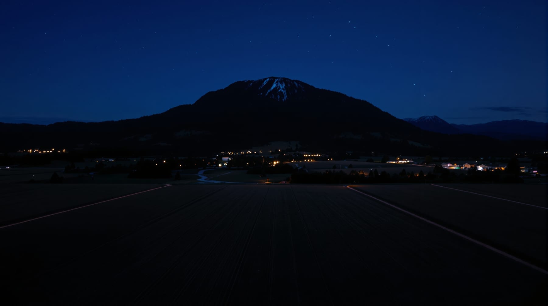 Farmland and a forested mountain at twilight with a dark park clearing at its base