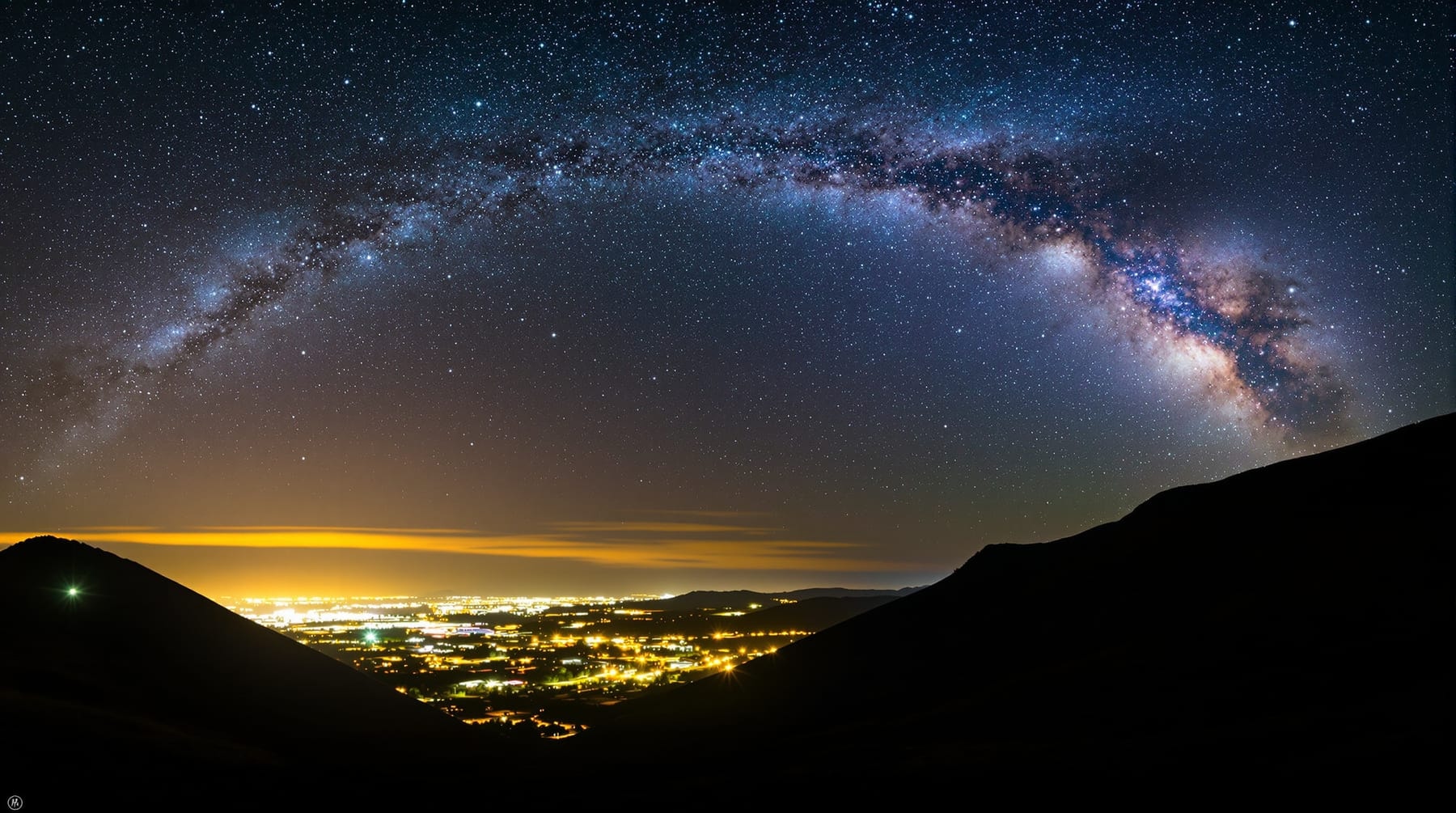 A city light dome on one side of the sky and a rich star field on the other