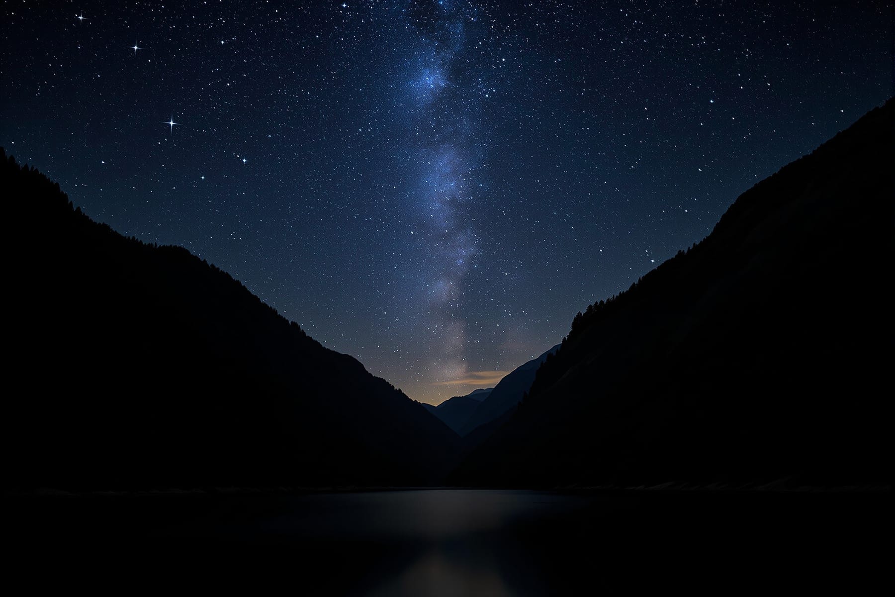 A narrow strip of starry sky between steep forested ridges above a still mountain lake
